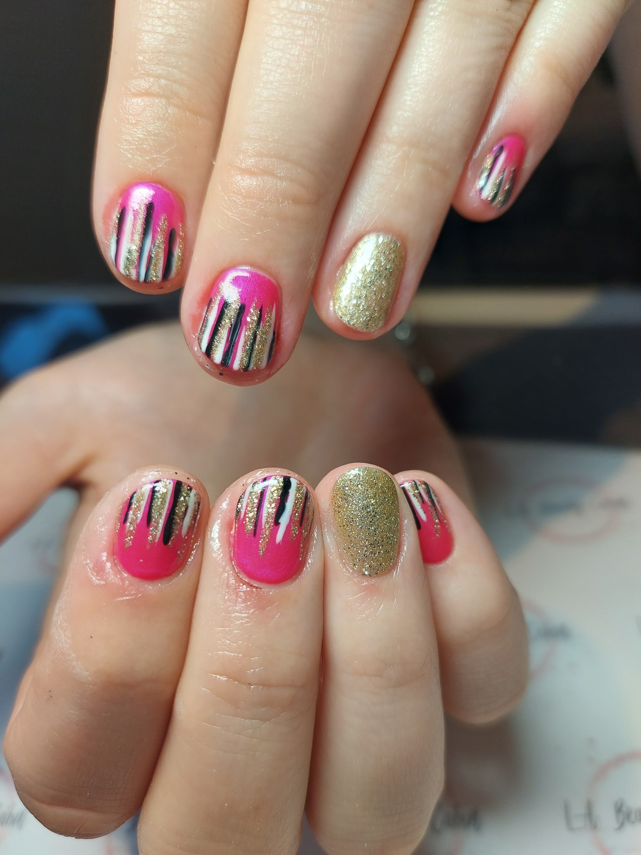 Pink nails with gold glitter and black and white striped details