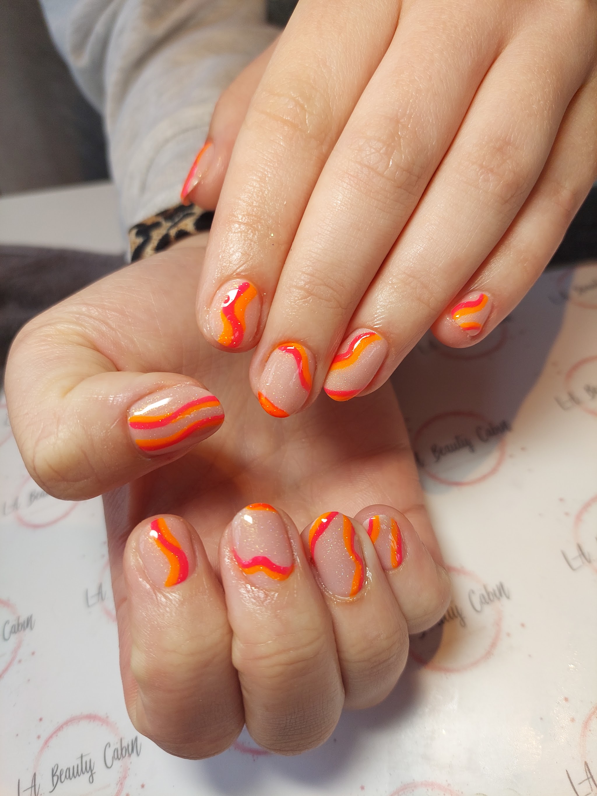 Nails with flowing orange and pink swirls on a soft neutral base